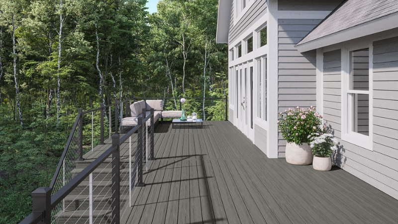 Gray deck beside a house with potted plants, overlooking a wooded landscape and fenced slope