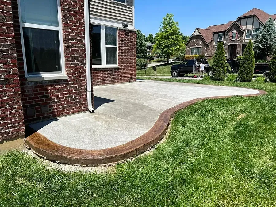 Concrete front porch with a curved brick edge beside a grassy lawn at a house entrance