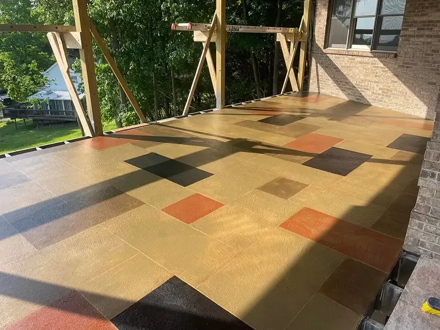 Sunlit outdoor terrace with multicolored square tile pattern and wooden railing beside a building