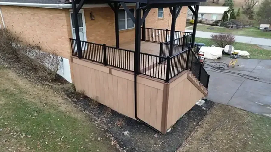Covered porch ramp with black railing and tan panels beside a brick building and driveway