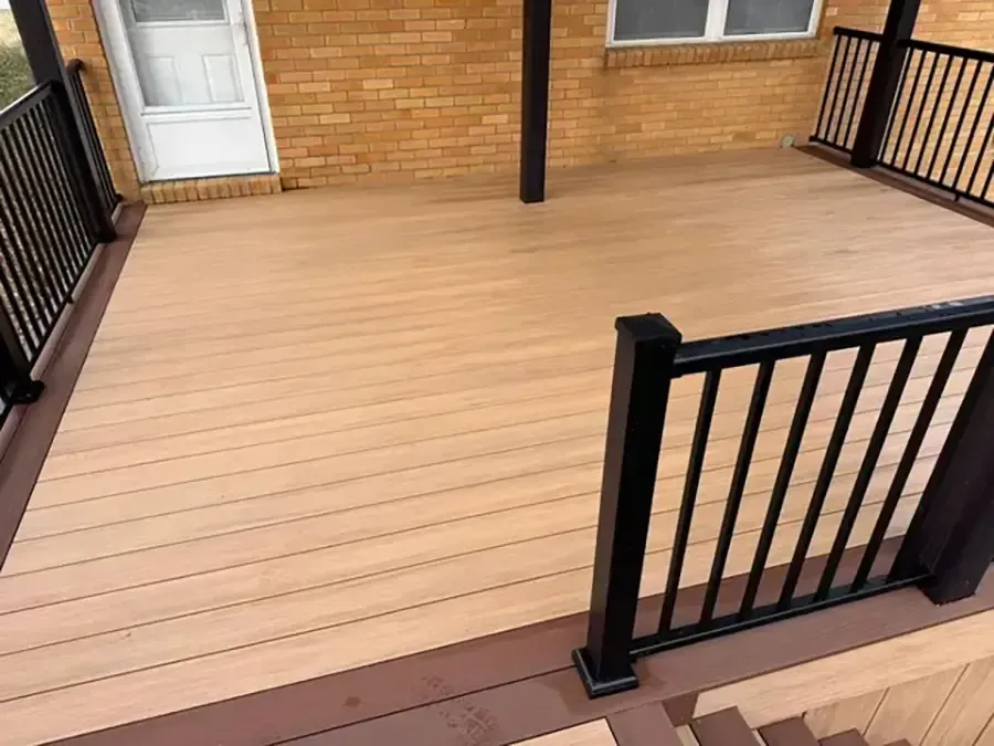 Empty tan wooden deck with black railings and a white door on a brick house.