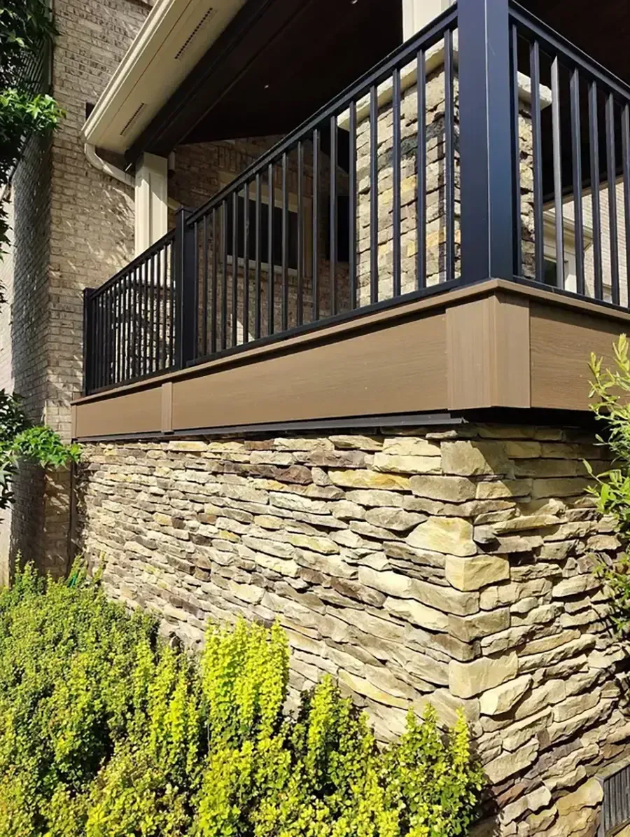 Stone house porch with black metal railing, beige trim, and shrubs in front