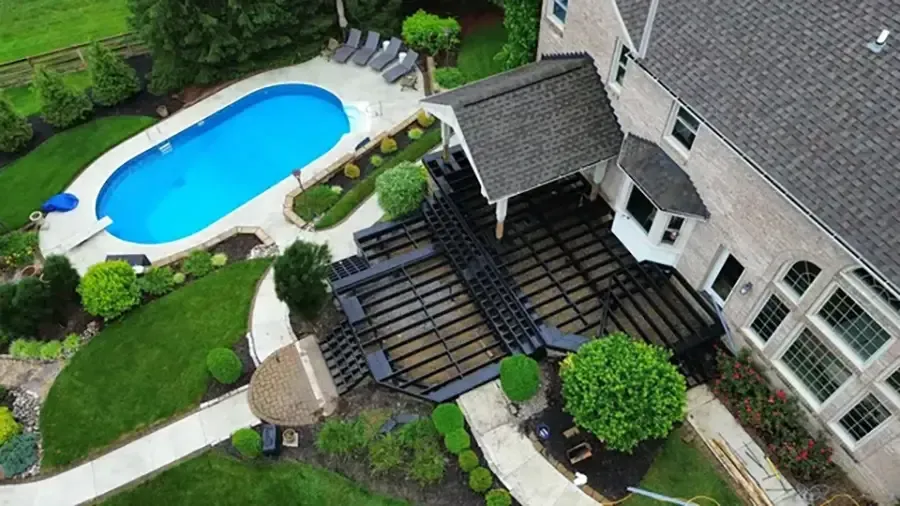 Aerial view of a backyard with a blue swimming pool, patio seating, and a house with a stone exterior