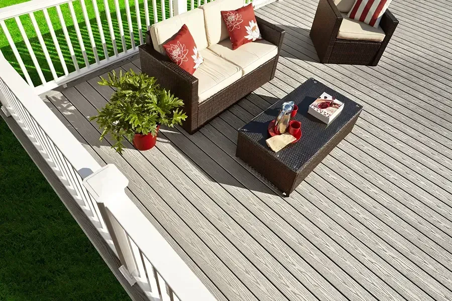 Outdoor deck with beige wicker seating, dark coffee table, red pillows, and a potted plant on gray boards