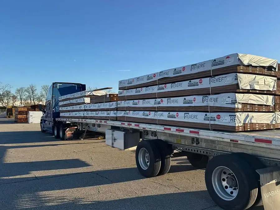 Flatbed trailer carrying wrapped lumber bundles in an outdoor yard under a clear blue sky