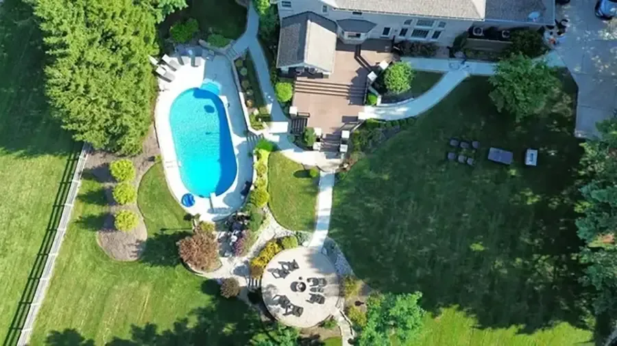 Aerial view of a backyard with a turquoise pool, patio seating, and a house surrounded by green lawn.