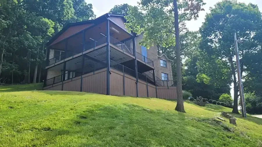 Wooden cabin with screened porch on a grassy hillside surrounded by trees