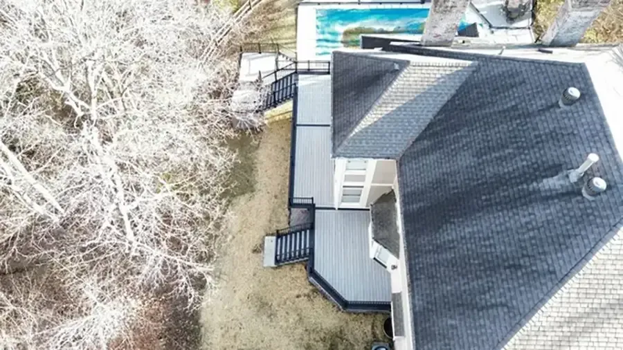 Aerial view of a gray-roofed house beside trees, lawn, and a backyard pool.