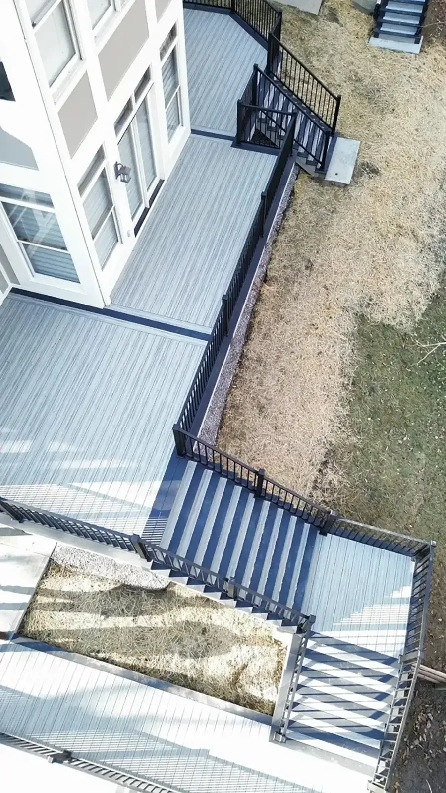 Aerial view of a house deck with black railings, stairs, and a gravel yard below.