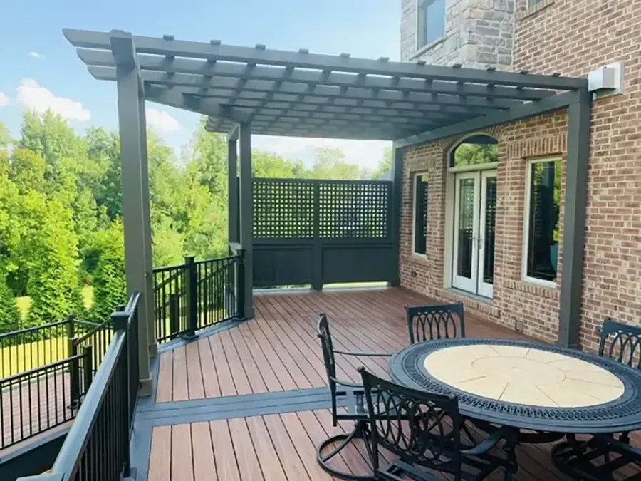 Backyard deck with pergola, black railing, and round table beside a brick house