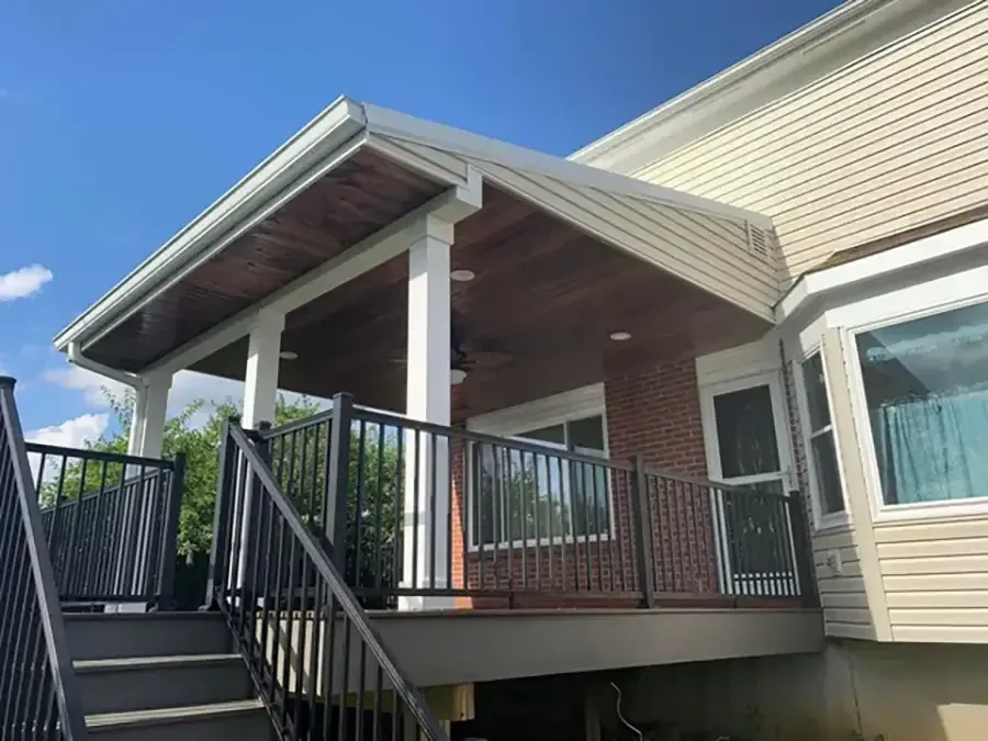 Covered porch with black railing and stairs on a beige house under a blue sky