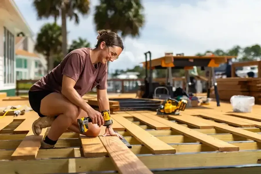 Worker measuring wooden planks on a construction site with tools and pallets nearby