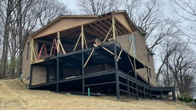 Partially built hillside house with exposed framing and wraparound deck among leafless trees