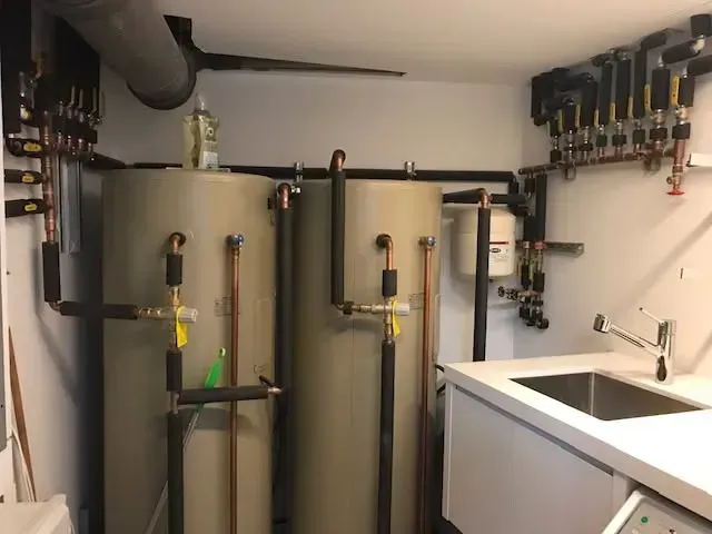 Boiler room with two large tanks, pipes, valves, and a sink in a utility space