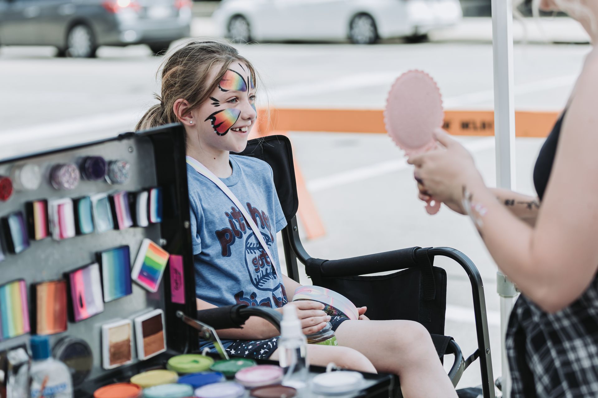 A girl is sitting in a chair getting her face painted.