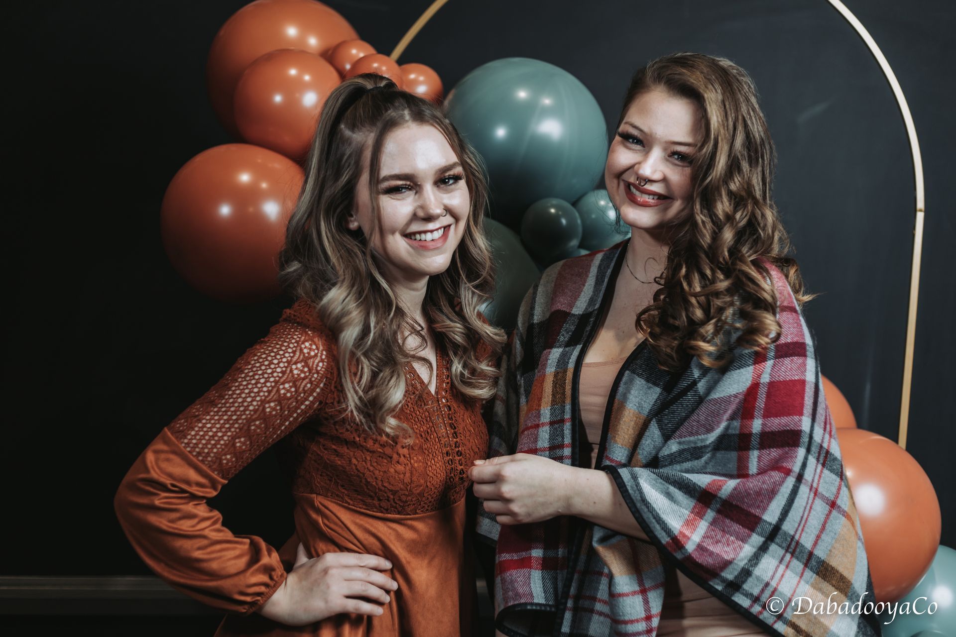 Two women are posing for a picture in front of balloons.