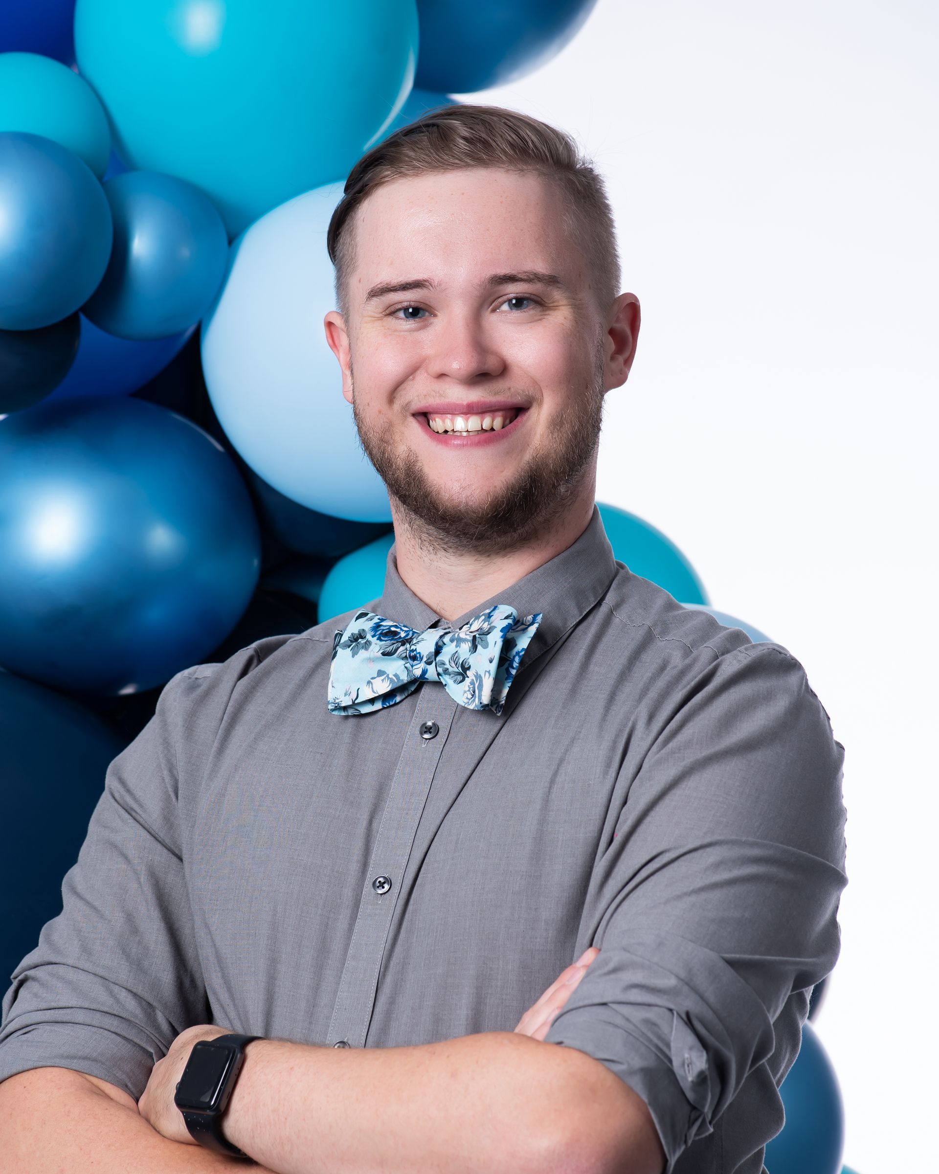 A man wearing a bow tie is standing in front of blue balloons.