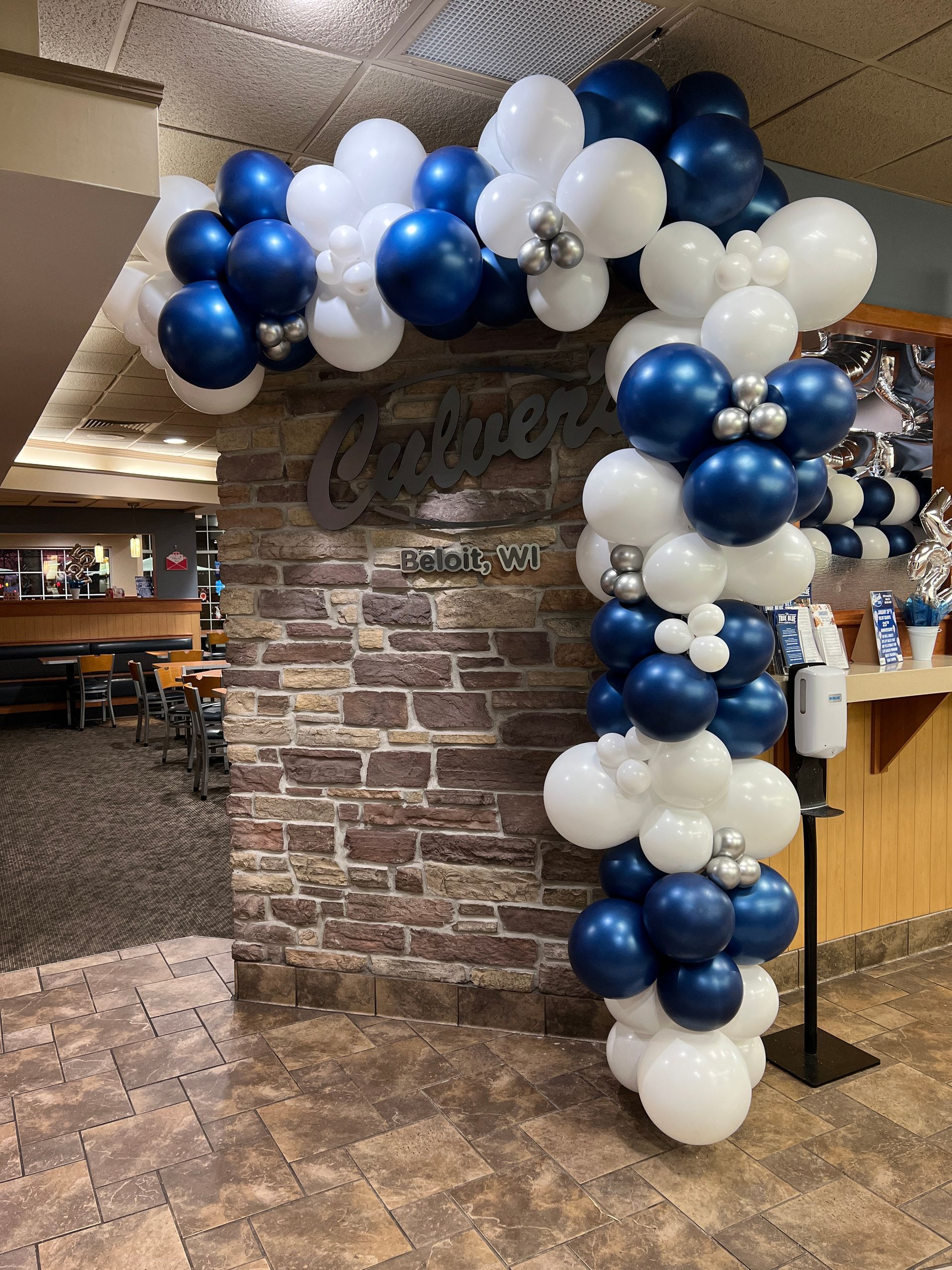 A brick wall is decorated with blue and white balloons.