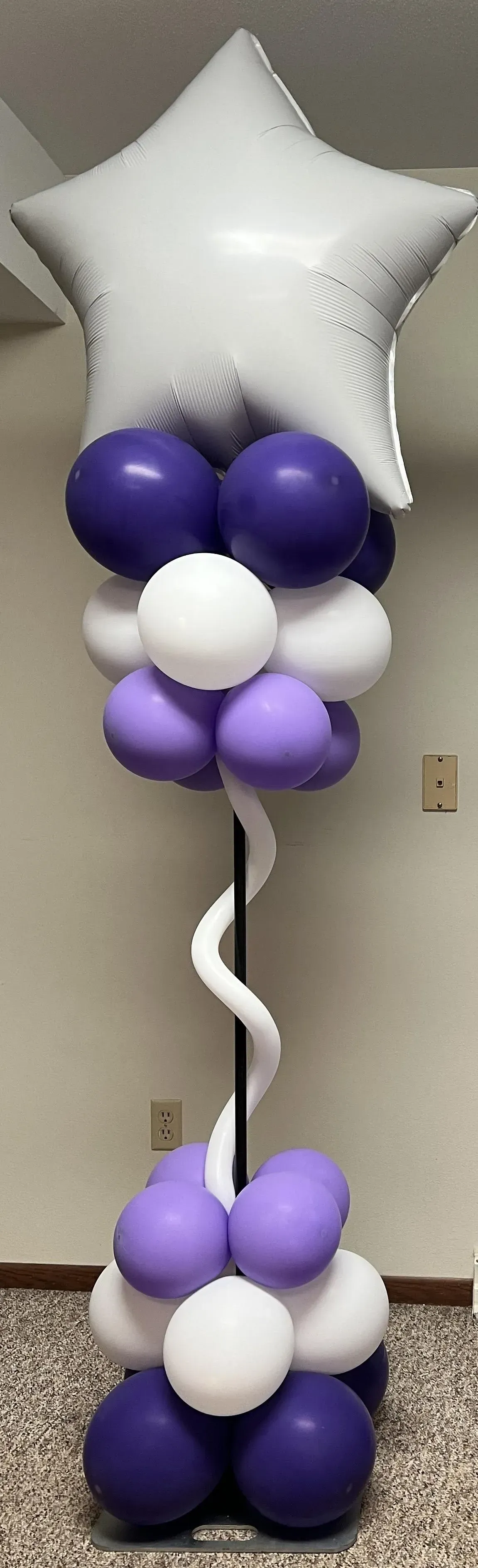 A purple and white balloon tower with a white star in the middle.