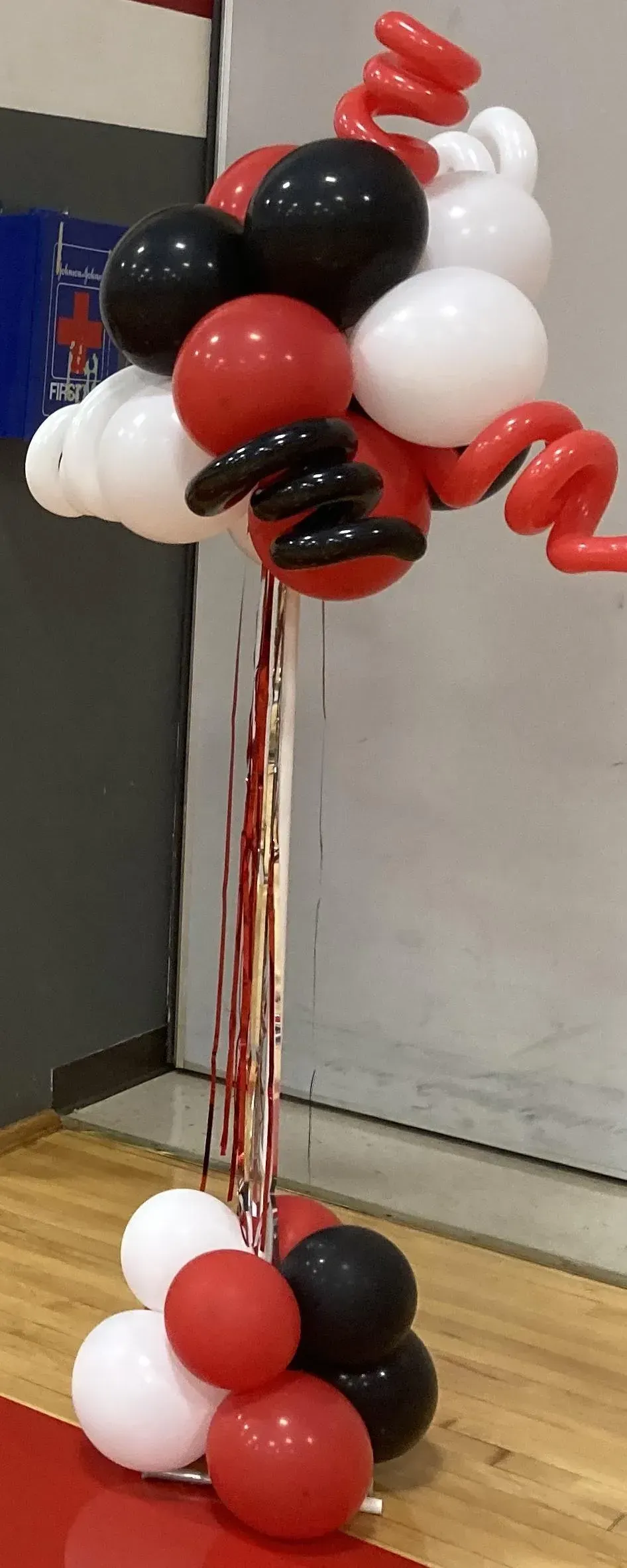 A bunch of red , white and black balloons sitting on top of a wooden floor.