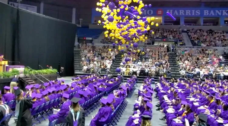 A graduation ceremony with purple and yellow balloons being thrown in the air