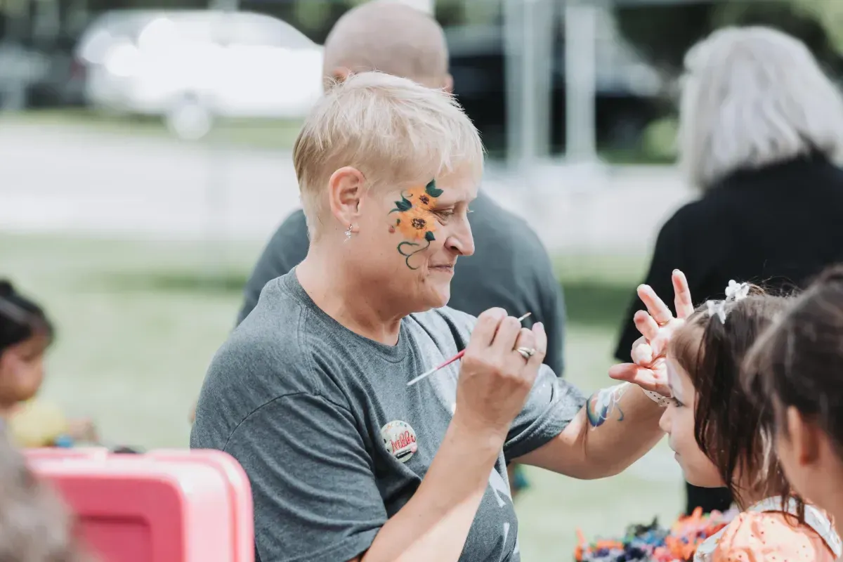 A woman is painting a child 's face at a park.