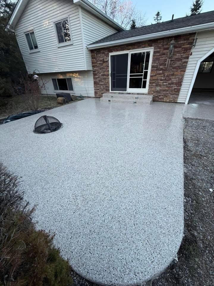 Freshly poured gray concrete patio beside a house with a basement window well and gravel edge