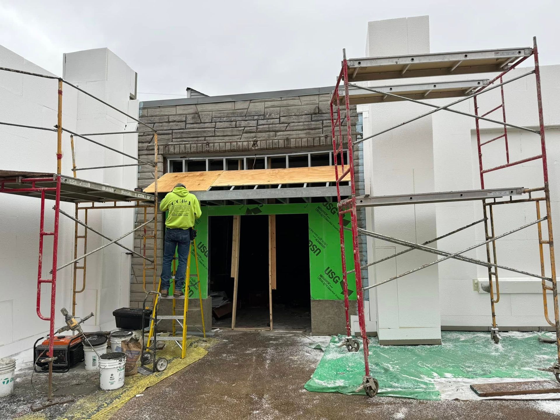 Construction workers on scaffolding painting a building entrance green, with unfinished facade above.