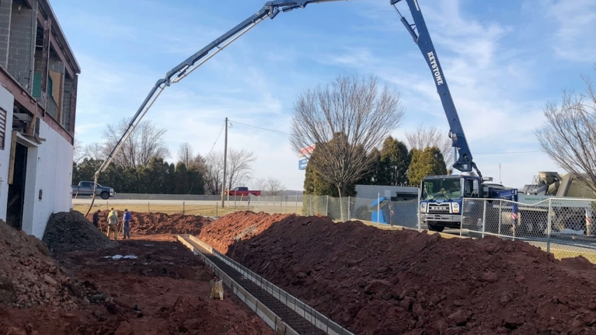 Concrete pump boom pouring at a construction site beside a building and dirt piles