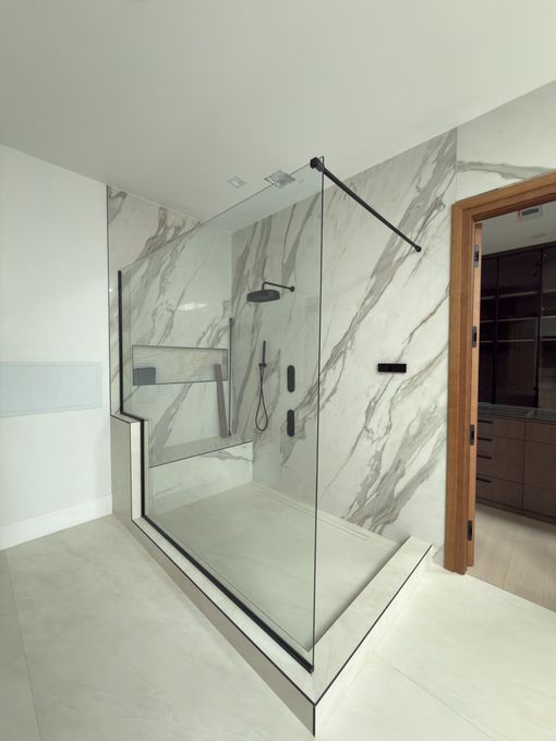 Glass walk-in shower with marble-look tile walls and a black rainfall showerhead in a bright bathroom