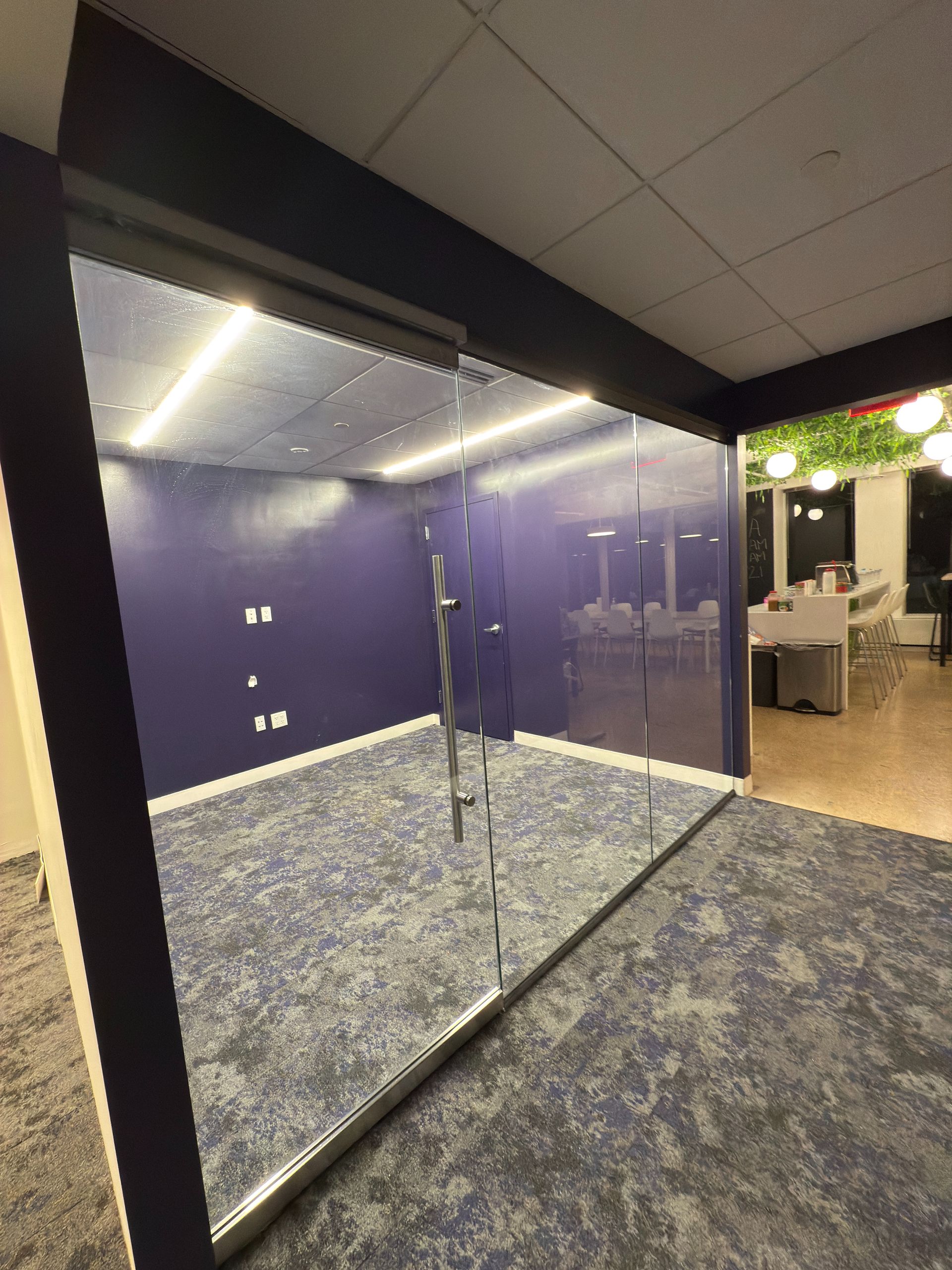 Modern open office with desks, computers, glass walls, and a carpeted hallway leading to windows.