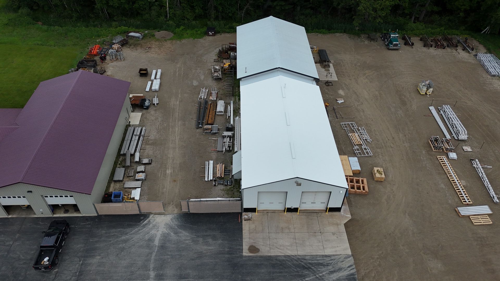 Aerial view of two buildings with a variety of construction materials and equipment on a gravel lot.