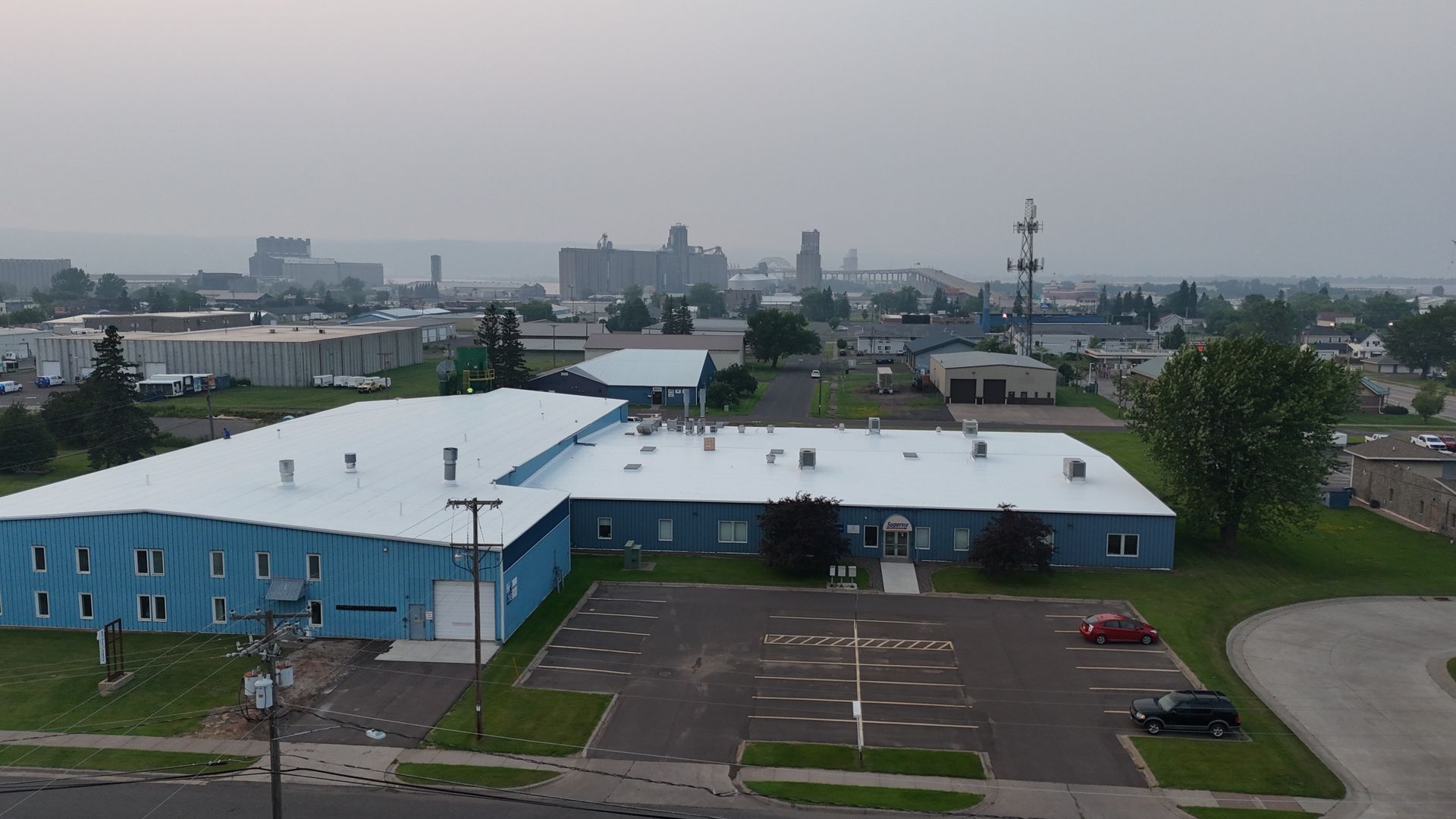 Blue industrial buildings with parking lot in a hazy urban setting.