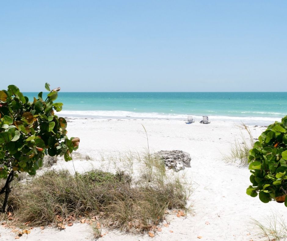 Sandy beach with white sand, turquoise water, and two lounge chairs under a clear blue sky.