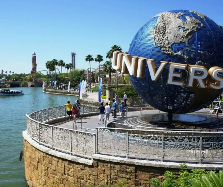 Universal globe sign at a theme park with visitors and palm trees by the water