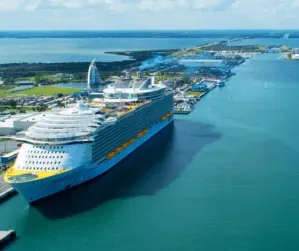 Aerial view of a tropical cruise port with three ships docked in turquoise water near a sandy island.