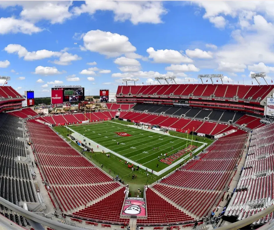 Empty red football stadium with green field under a blue sky with clouds