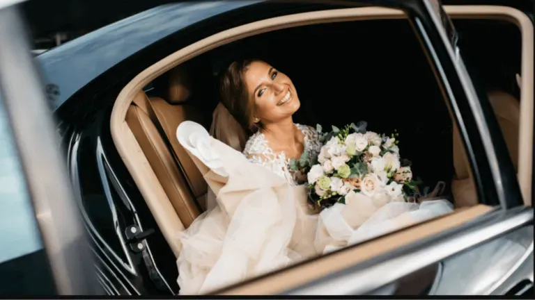 Bride smiling in a car, holding a bouquet and wearing a white wedding dress