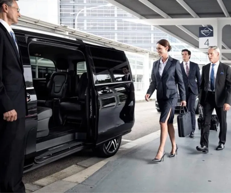 Business travelers walking beside a black van at an airport curbside pickup area