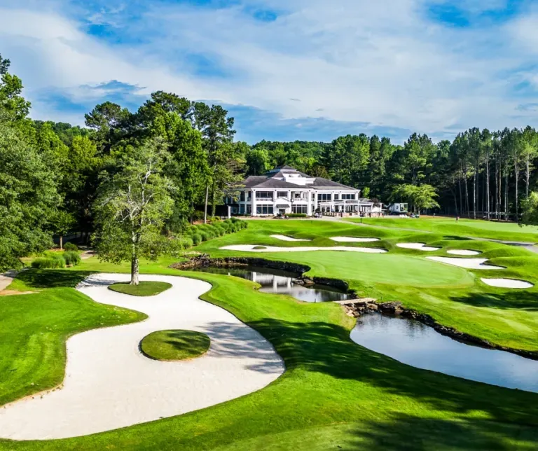 Golf course with white sand bunkers, bright green fairways, water features, and a clubhouse in the distance