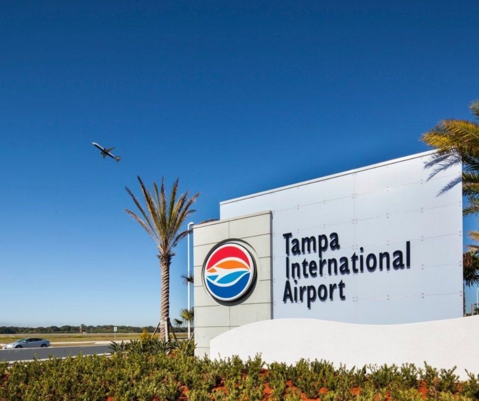 Tampa International Airport sign with logo under a clear blue sky and a small airplane overhead