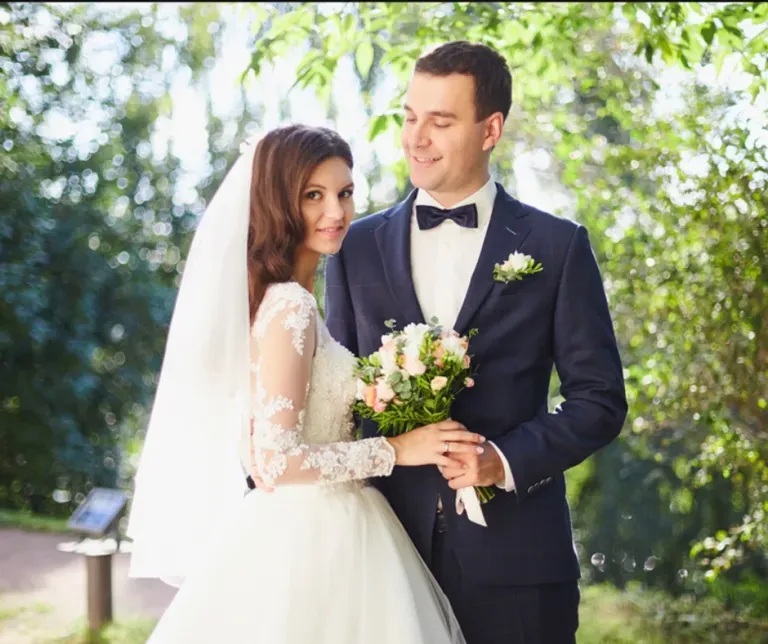 Bride and groom posing outdoors, smiling and holding a bouquet at their wedding ceremony