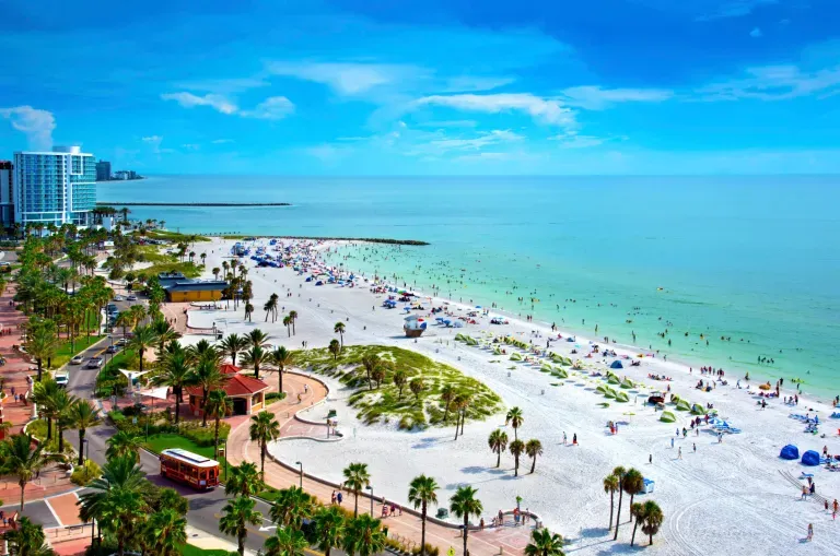 Sunny beach resort with white sand, turquoise water, palm trees, and people relaxing on the shore