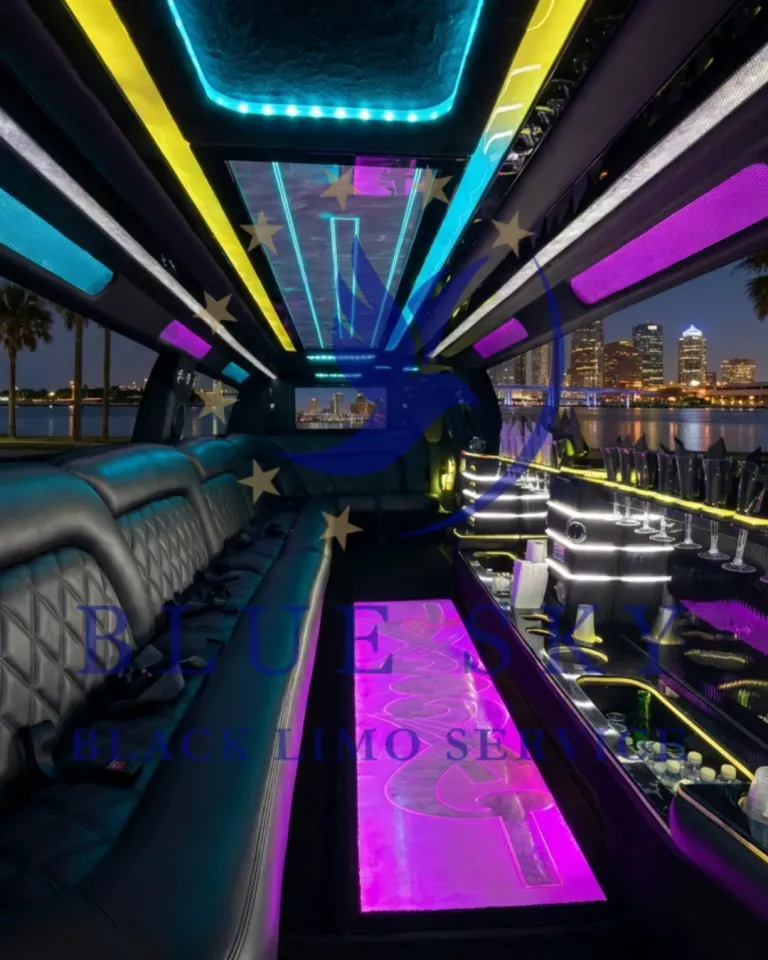 Neon-lit party bus interior with colorful LED ceiling, leather seats, and city lights outside