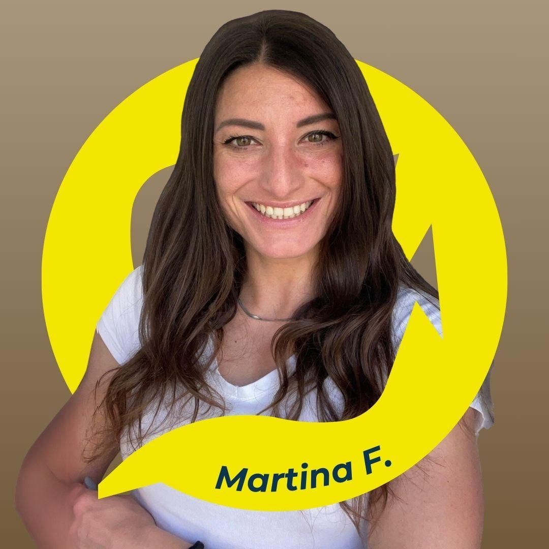 Martina F. sorride davanti a un vortice giallo, indossando una maglietta bianca, su uno sfondo marrone.