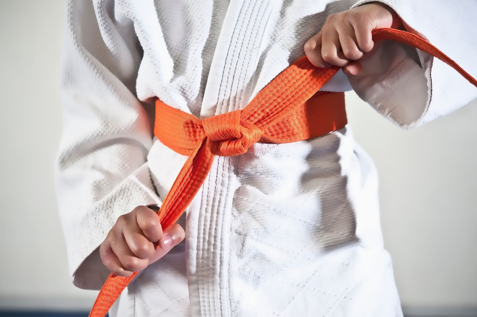 Bambino che allaccia una cintura arancione a un'uniforme bianca da judo.