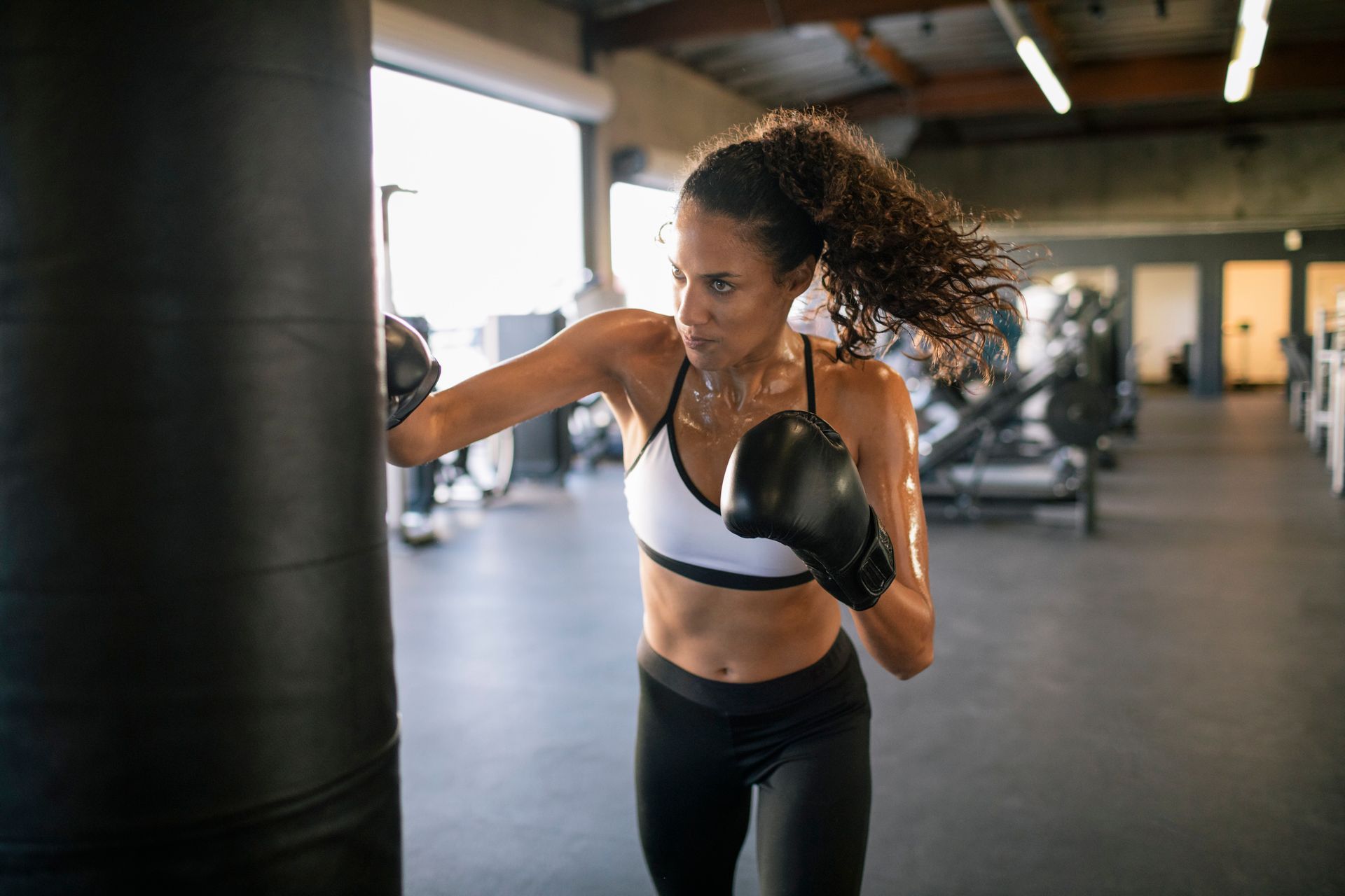 Una donna in palestra solleva un sacco pesante; è sudata e concentrata.