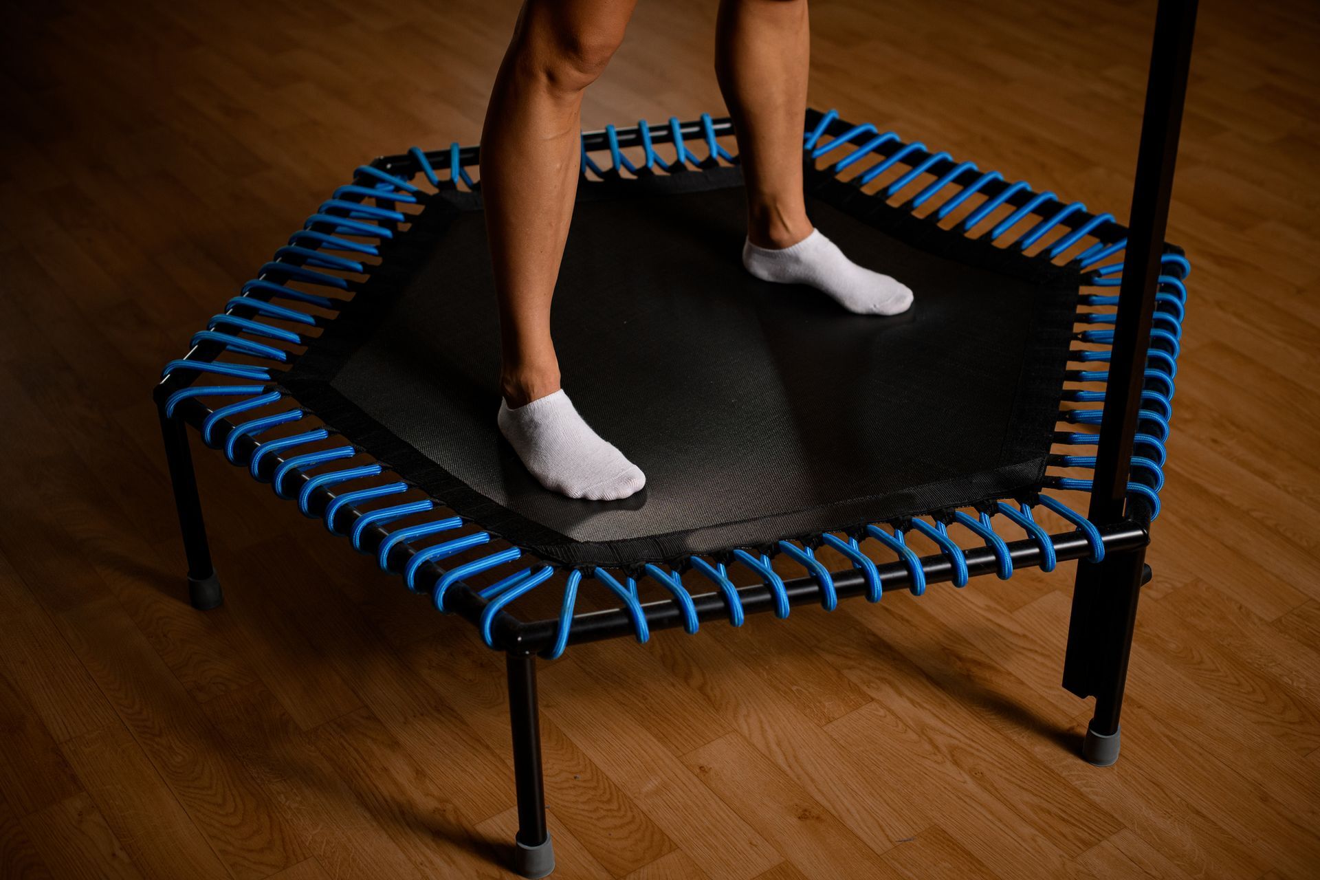 Persona che rimbalza su un piccolo trampolino esagonale; dettagli blu, pavimento in legno.