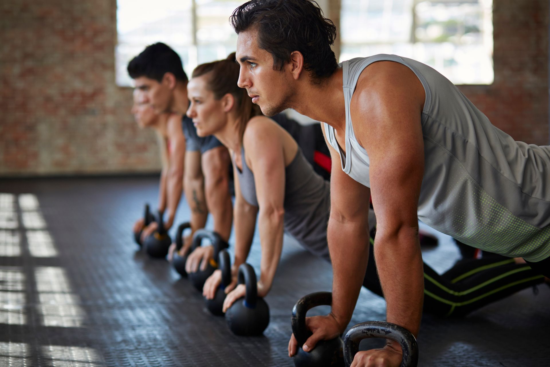 Persone in abbigliamento sportivo che fanno flessioni con i kettlebell sul pavimento di una palestra.