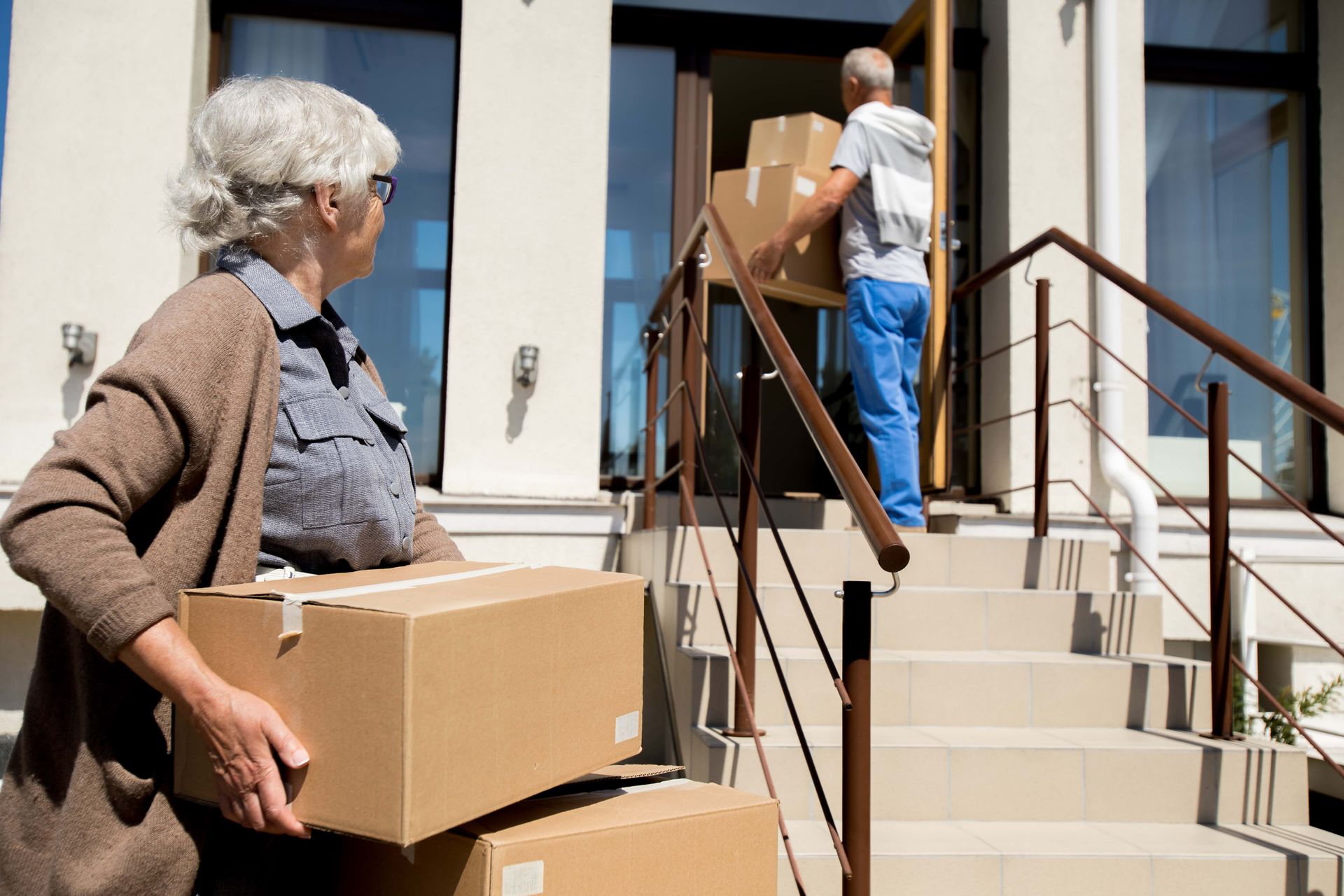 Two people carrying cardboard boxes up the steps of a house during a move